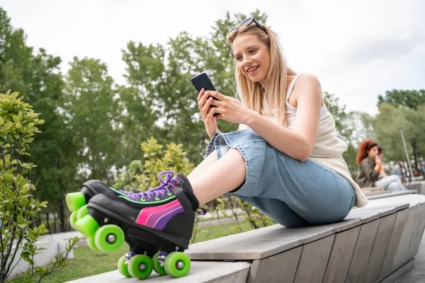 Happy Blonde Woman Rollers Skates Sitting Border Bench Messaging Cellphone — Stock Photo, Image
