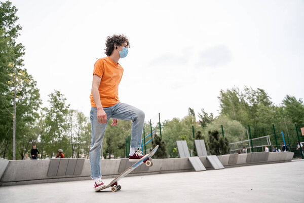 молодой человек в медицинской маске катается на скейтборде в скейт-парке