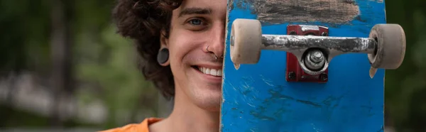 Vreugdevolle Jongeman Obscurerend Gezicht Met Skateboard Terwijl Hij Naar Camera — Stockfoto