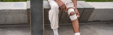 Sınır bankında otururken yaralı dizini saran Afro-Amerikan patenci görüntüsü