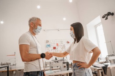 Tıp maskeli ve atölyede el sıkışan çok ırklı tasarımcıların yan görünüşü 