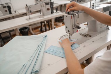 Atölyedeki kumaşın yanında tıbbi maske diken terzi manzarası. 