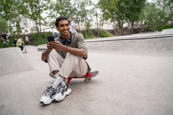 Young Happy African American Man Using Smartphone While Sitting Skateboard — Stock Photo, Image