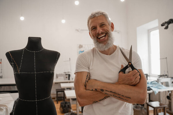Cheerful designer with scissors looking at camera near mannequin 