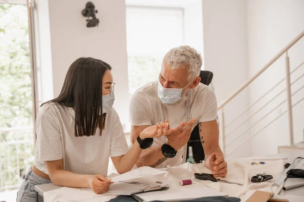 Diseñadores Multiétnicos Máscaras Médicas Hablando Cerca Tela —  Fotos de Stock