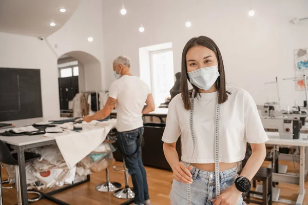 Asiático Designer Com Máscara Médica Fita Métrica Olhando Para Câmera — Fotografia de Stock