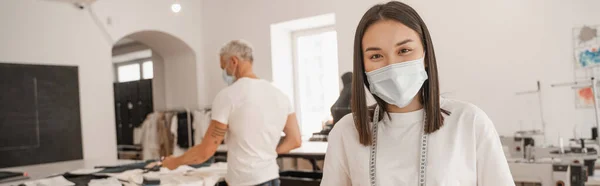 Designer Asiático Máscara Médica Olhando Para Câmera Enquanto Colega Borrado — Fotografia de Stock