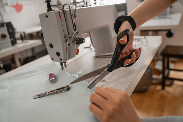 Cropped view of seamstress cutting cloth near sewing machine 