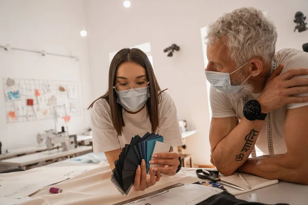 Asiatischer Designer Medizinischer Maske Hält Farbmuster Neben Kollegin Stockfoto