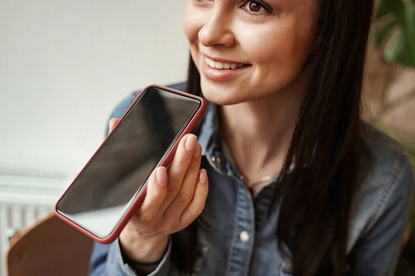 Cheerful young woman recording voice message while holding smartphone — Stock Photo