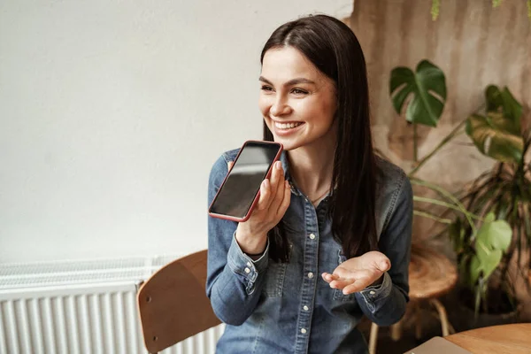 Sorridente giovane donna che registra il messaggio vocale mentre tiene lo smartphone — Foto stock