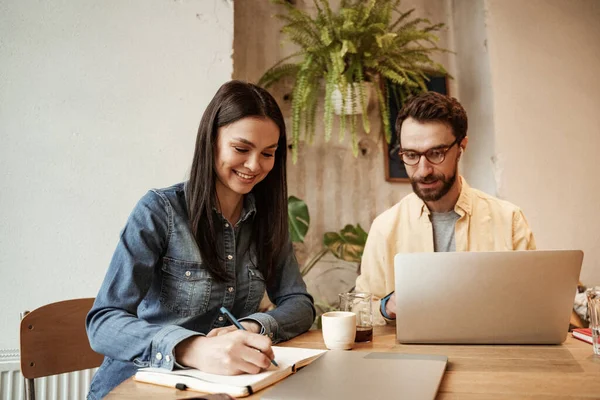 Freelancers writing in notebook and using laptop in cafe — Stock Photo