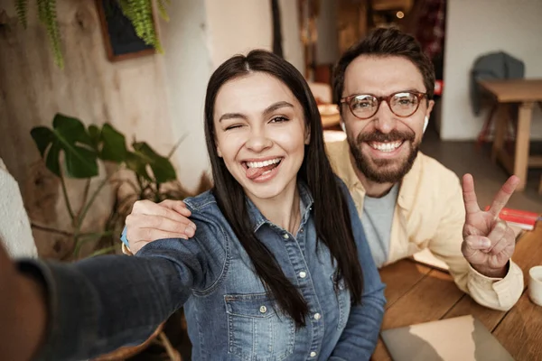 Cheerful woman sticking out tongue near man showing peace sign — Stock Photo