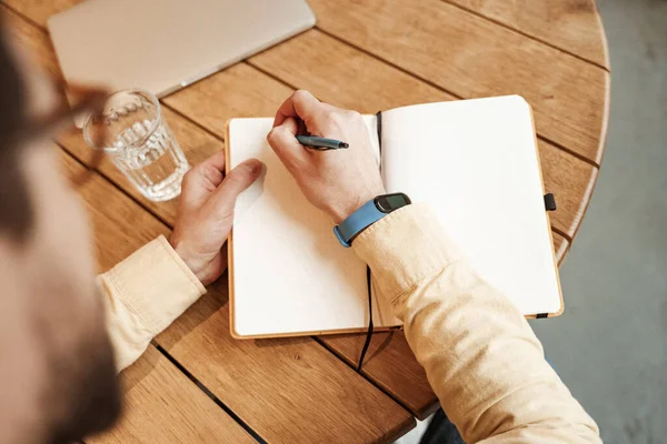High angle view of freelancer with smart watch on hand writing in notebook — Stock Photo