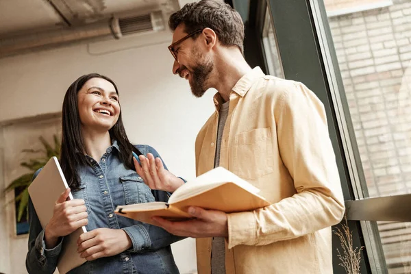 Vista de ángulo bajo del hombre barbudo sosteniendo el cuaderno mientras habla con la mujer alegre - foto de stock