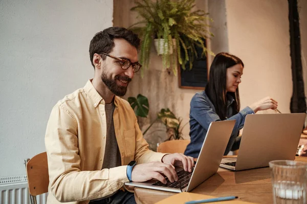 Bearded freelancer typing on laptop near woman on blurred background — Stock Photo