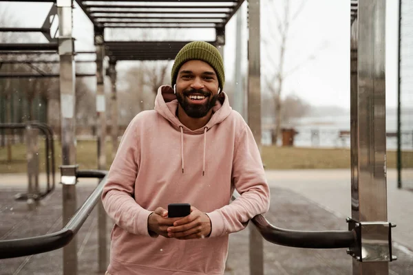 Happy african american sportsman listening music in wireless earphones on sports ground — Stock Photo