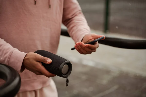 Cropped view of african american sportsman holding smartphone and portable music speaker on blurred background — Stock Photo