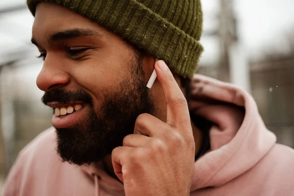 Smiling, bearded african american man adjusting earphone while listening music outdoors — Stock Photo