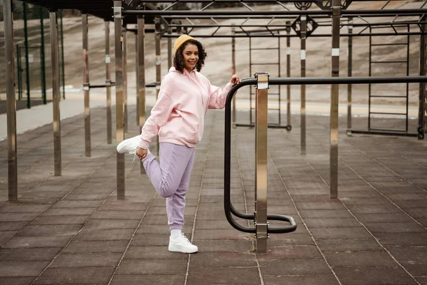 Юна афроамериканська спортсменка посміхається перед камерою, розтягуючись на спортивному майданчику. — стокове фото