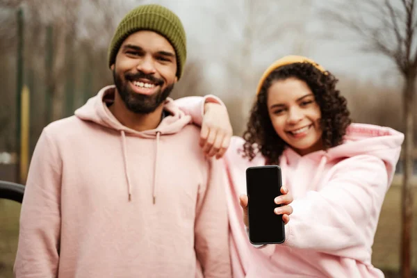 Happy african american sportswoman showing smartphone with blank screen near smiling friend, blurred background — Stock Photo