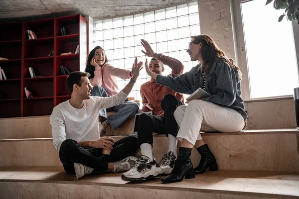 Happy interracial students smiling while giving high five and sitting on stairs, senior 2021 — Stock Photo