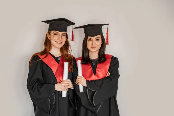 Pretty students in graduation gowns and caps holding paper rolls diploma, senior 2021 — Stock Photo
