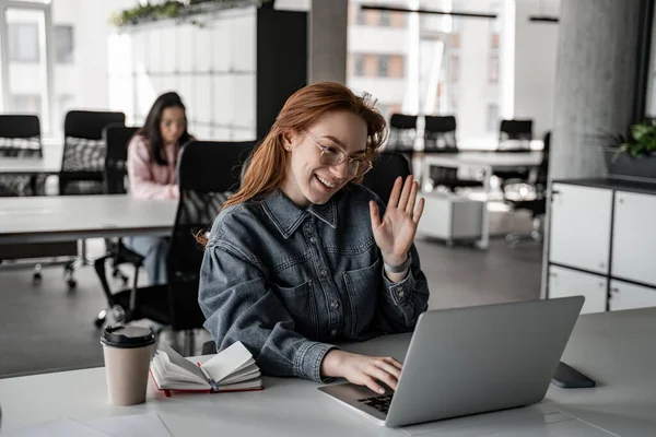 Cheerful redhead student waving hand while having video chat on laptop — Stock Photo