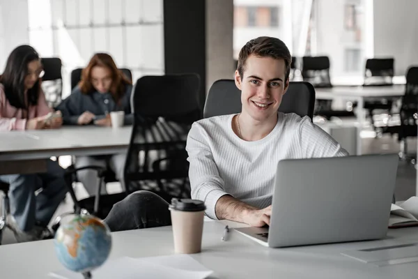 Étudiant heureux en utilisant ordinateur portable et tasse en papier et globe sur la table — Photo de stock