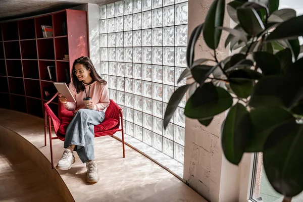 Glückliche junge Studentin in Gläsern mit Pappbecher und Coffee to go und E-Book lesen — Stockfoto