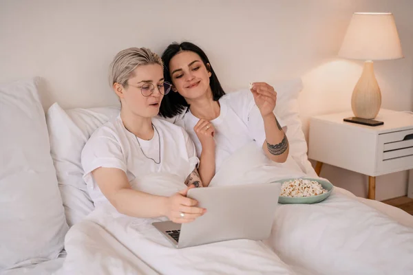 Glücklich brünette Frau hält Popcorn in der Nähe Freundin in Gläser, während Film auf Laptop — Stockfoto