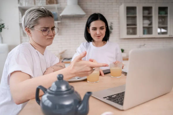 Lesbian woman in glasses pointing at laptop near blurred girlfriend — Stock Photo
