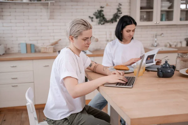 Татуированная женщина с помощью ноутбука рядом с подругой на размытом фоне — стоковое фото