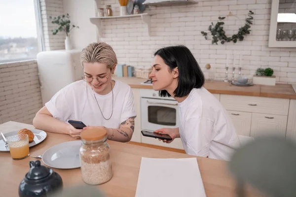 Happy lesbian couple using smartphones in kitchen — Stock Photo