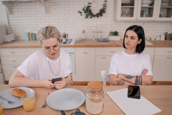 Displeased woman using smartphone near offended blurred girlfriend — Stock Photo