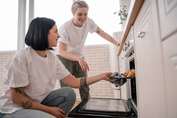 Happy lesbian couple near oven tray with homemade croissants in kitchen — Stock Photo