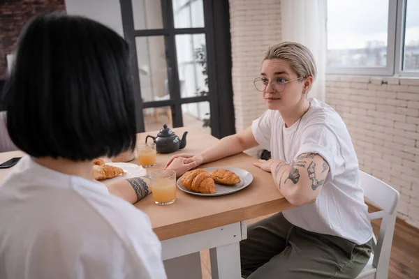 Tattooed lesbian couple holding hands and looking at each other in kitchen — Stock Photo