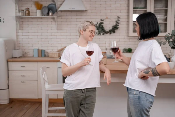 Feliz pareja lesbiana sosteniendo vasos de vino tinto en la cocina - foto de stock