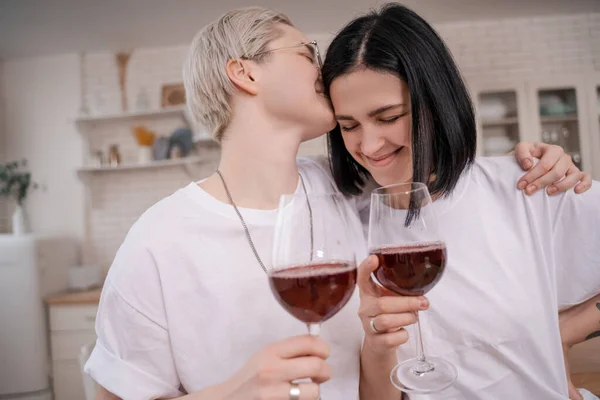 Frau in Gläsern küsst glückliche Freundin, während sie Rotweingläser hält — Stockfoto