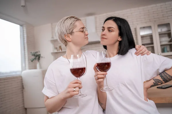Femme dans des lunettes étreignant petite amie tout en tenant des verres de vin rouge — Photo de stock