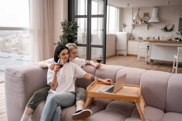Young lesbian couple watching movie on laptop while holding glasses of red wine in living room — Stock Photo
