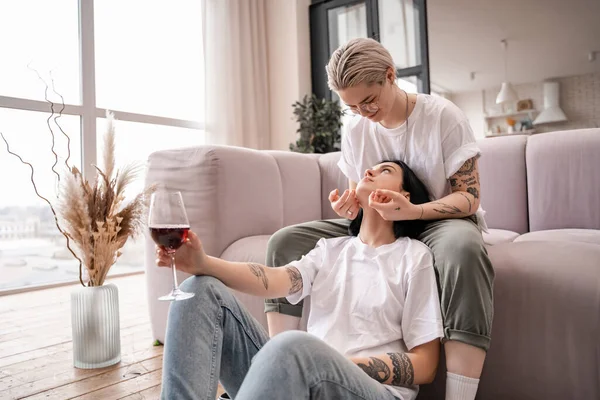 Donna tatuata guardando la ragazza con un bicchiere di vino rosso — Foto stock