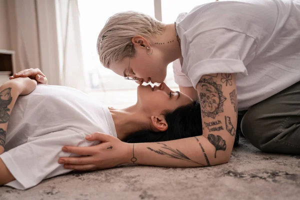 Side view of loving lesbian couple kissing on carpet — Stock Photo