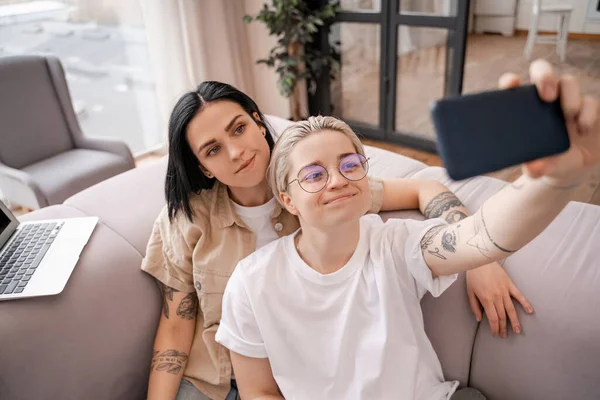 Mujer sonriendo con novia feliz en gafas tomando selfie en sala de estar - foto de stock