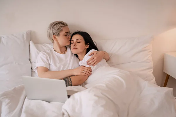 Jovem casal lésbico abraçando enquanto deitado na cama perto do laptop — Fotografia de Stock