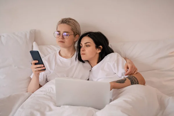 Junges lesbisches Paar liegt im Bett und schaut auf Smartphone neben Laptop — Stock Photo