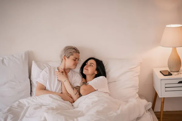 Smiling lesbian couple lying in bed and holding hands — Stock Photo