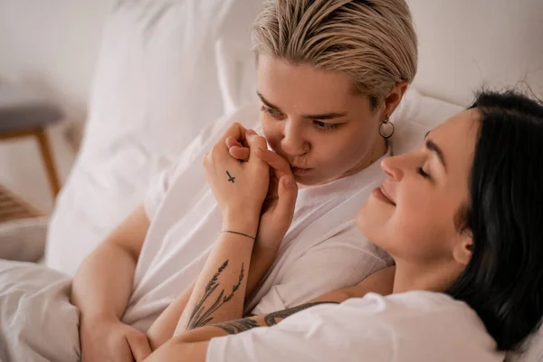 Молодая лесбийская пара, лежащая в постели и держащаяся за руки — стоковое фото