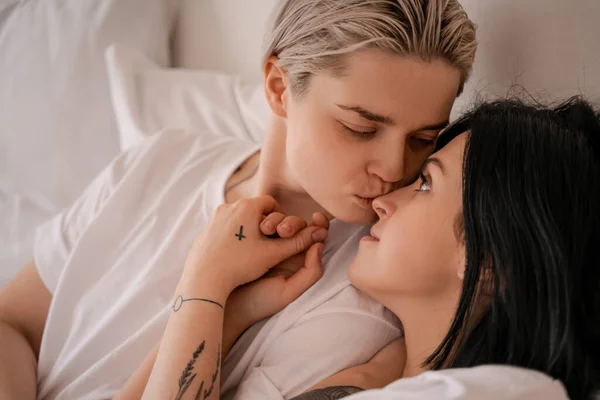 Young woman lying in bed and kissing nose of girlfriend — Stock Photo