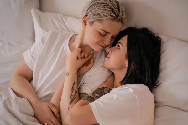 Loving young lesbian couple lying in bed and holding hands — Stock Photo